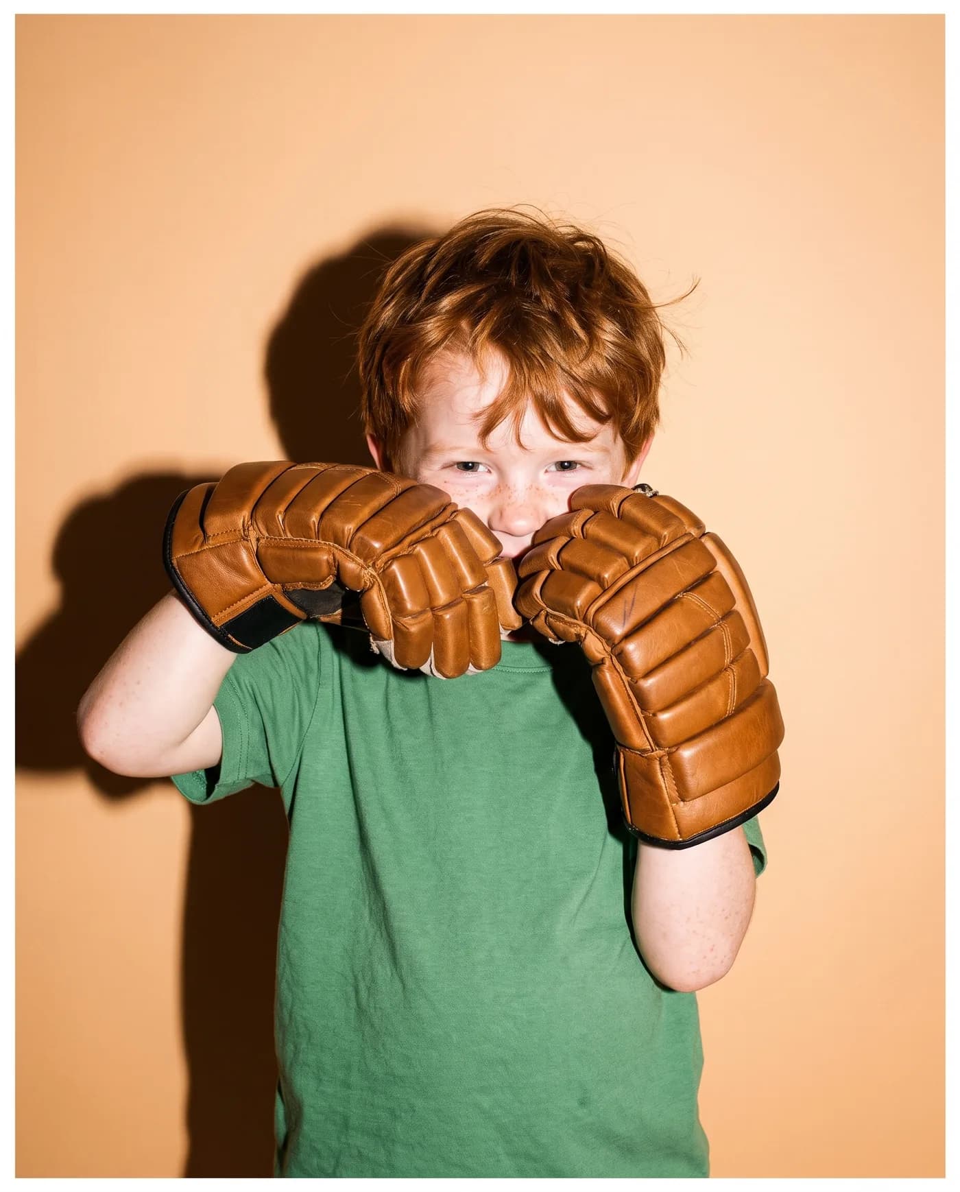 A boy on a peach backdrop peeks out between two big hockey gloves