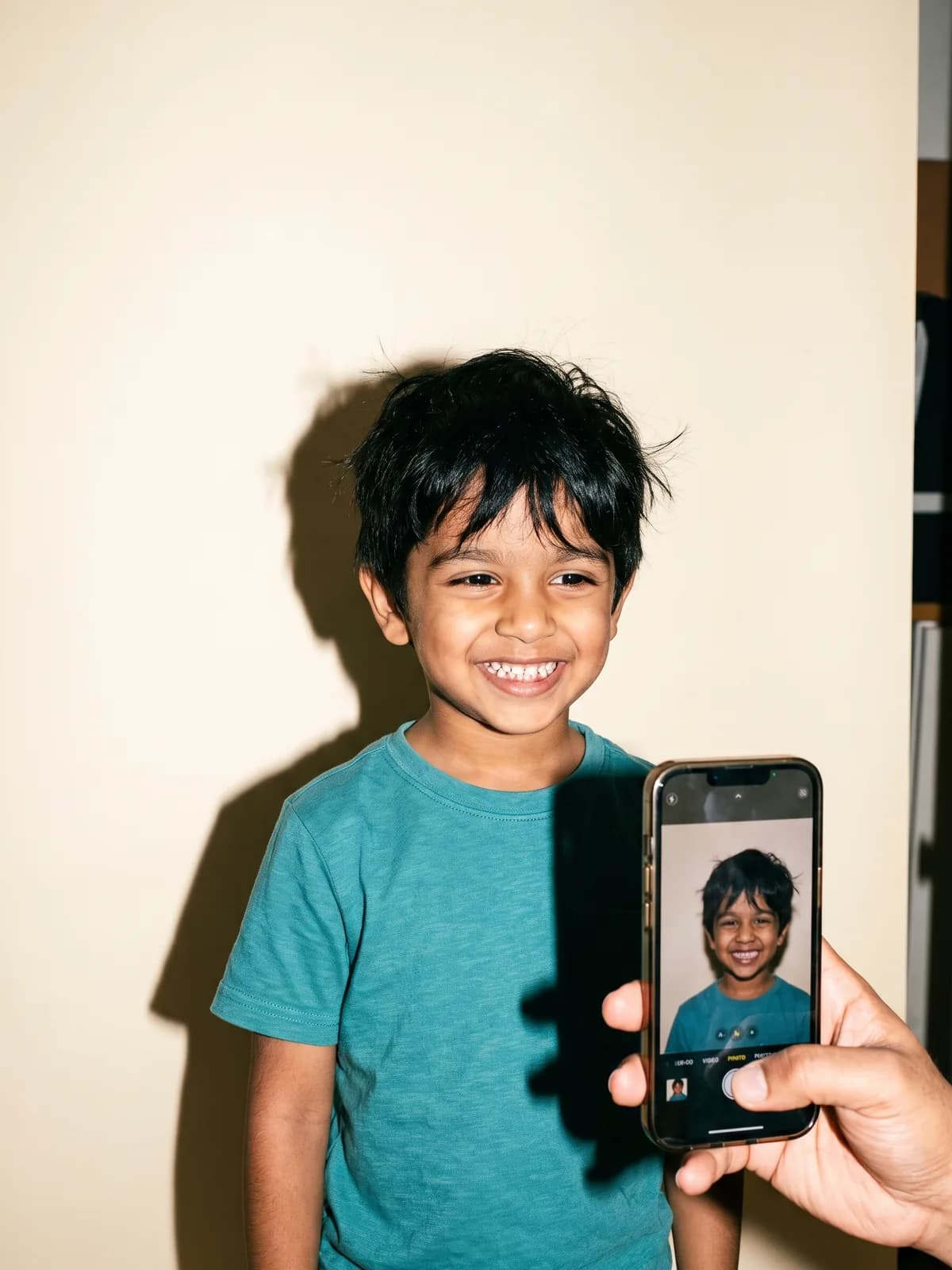 A parent’s phone photographs a grinning boy, Ravi, on a studio backdrop